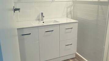 Un baño con tocador blanco, lavamanos y zona de ducha.