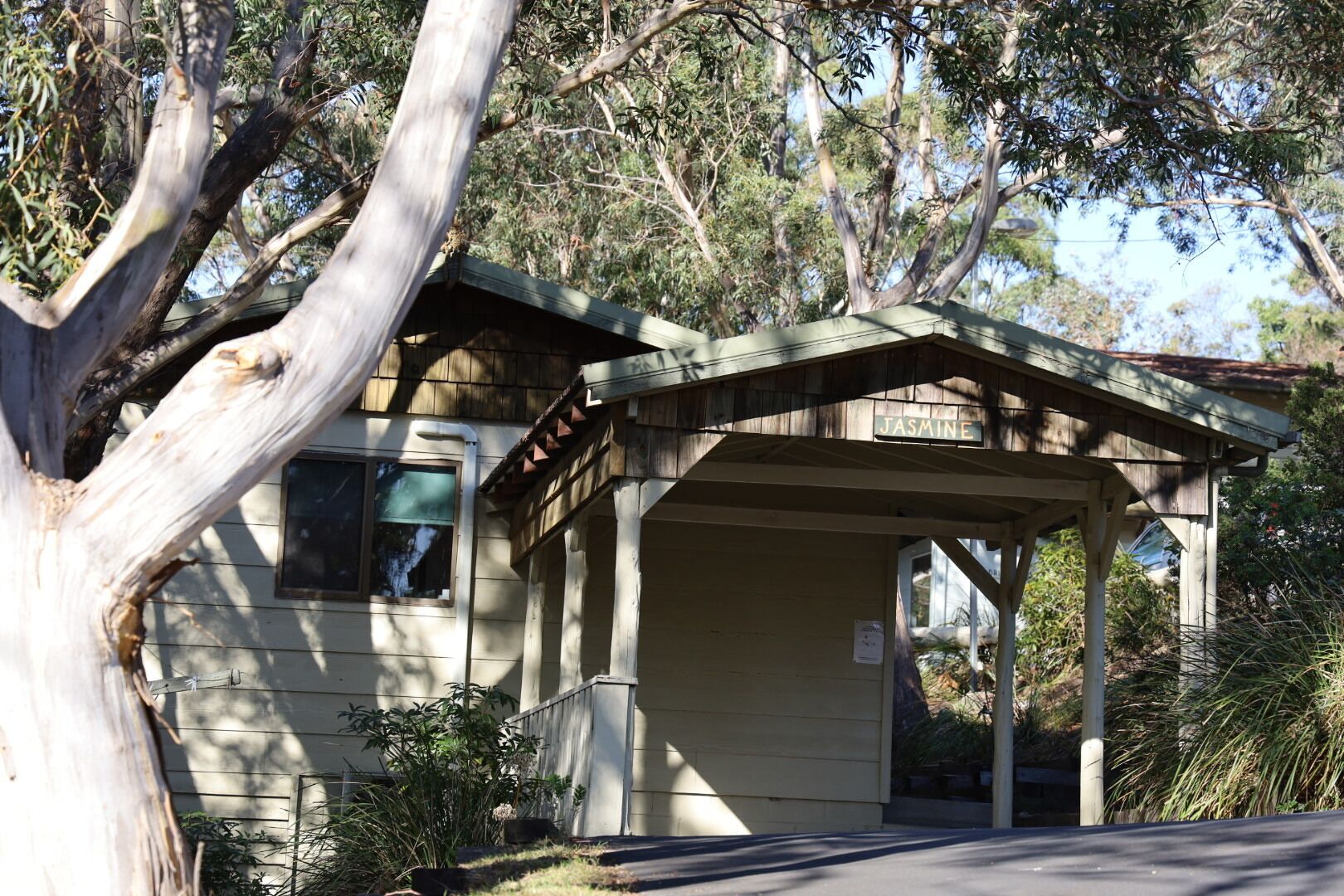 A small wooden structure with a sign reading "Jasmine" on a residential property surrounded by trees.