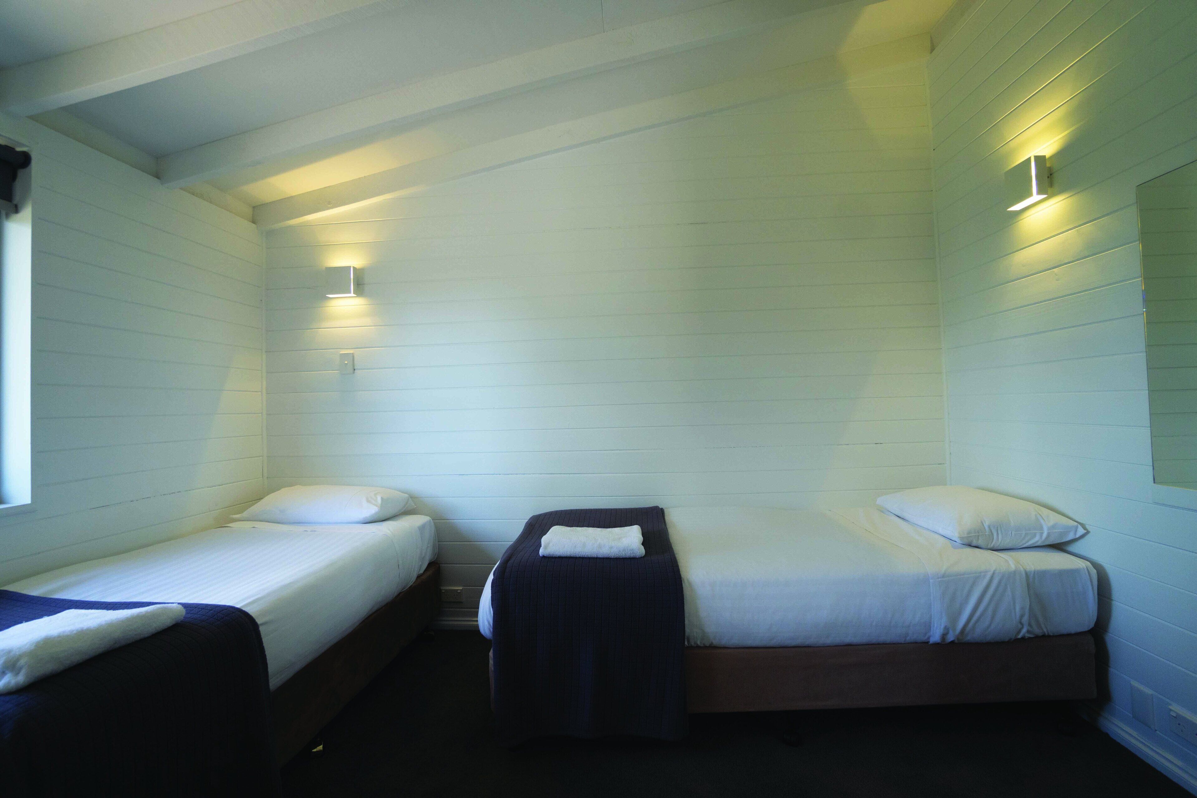 Un alojamiento pequeño y con una sola habitación, equipado con dos camas individuales, cada una con almohada y manta.