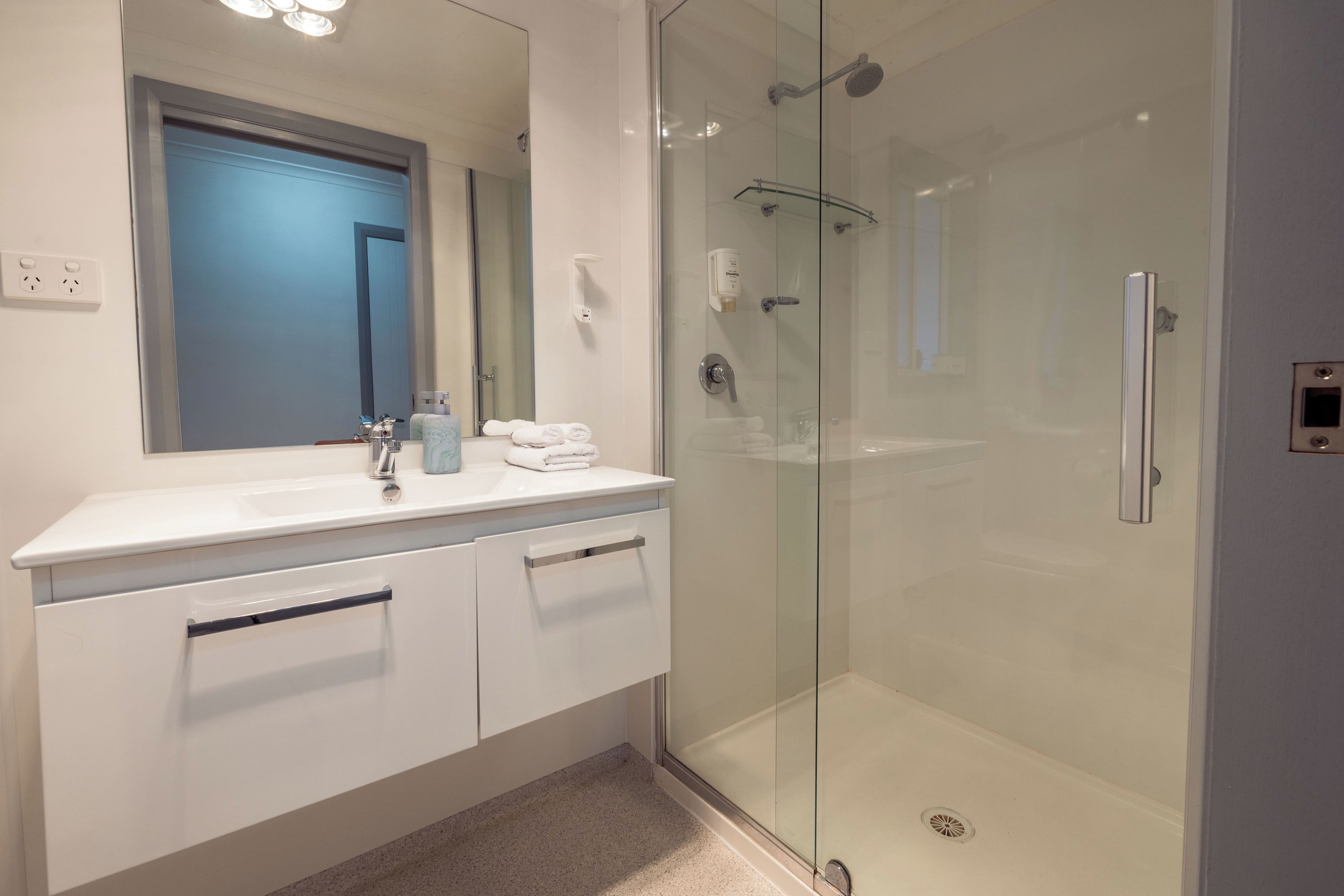 A modern bathroom with a glass shower enclosure, a white vanity with a mirror, and a blue door in the background.