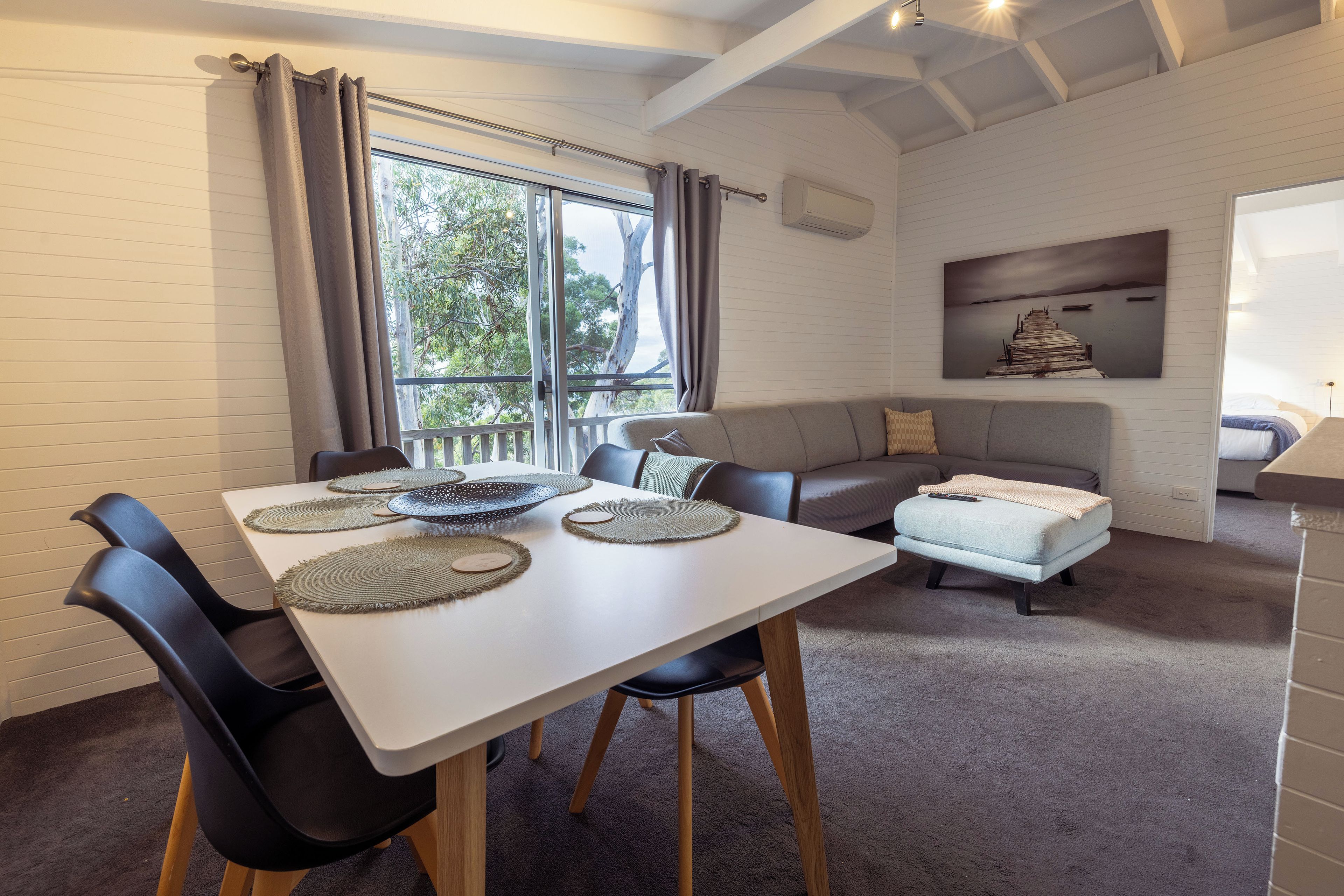 A modern living room with a dining area, featuring a white table, black chairs, and a grey sofa.