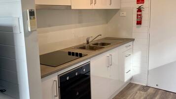 Una cocina moderna con armarios blancos, un lavamanos de acero inoxidable y un horno empotrado.