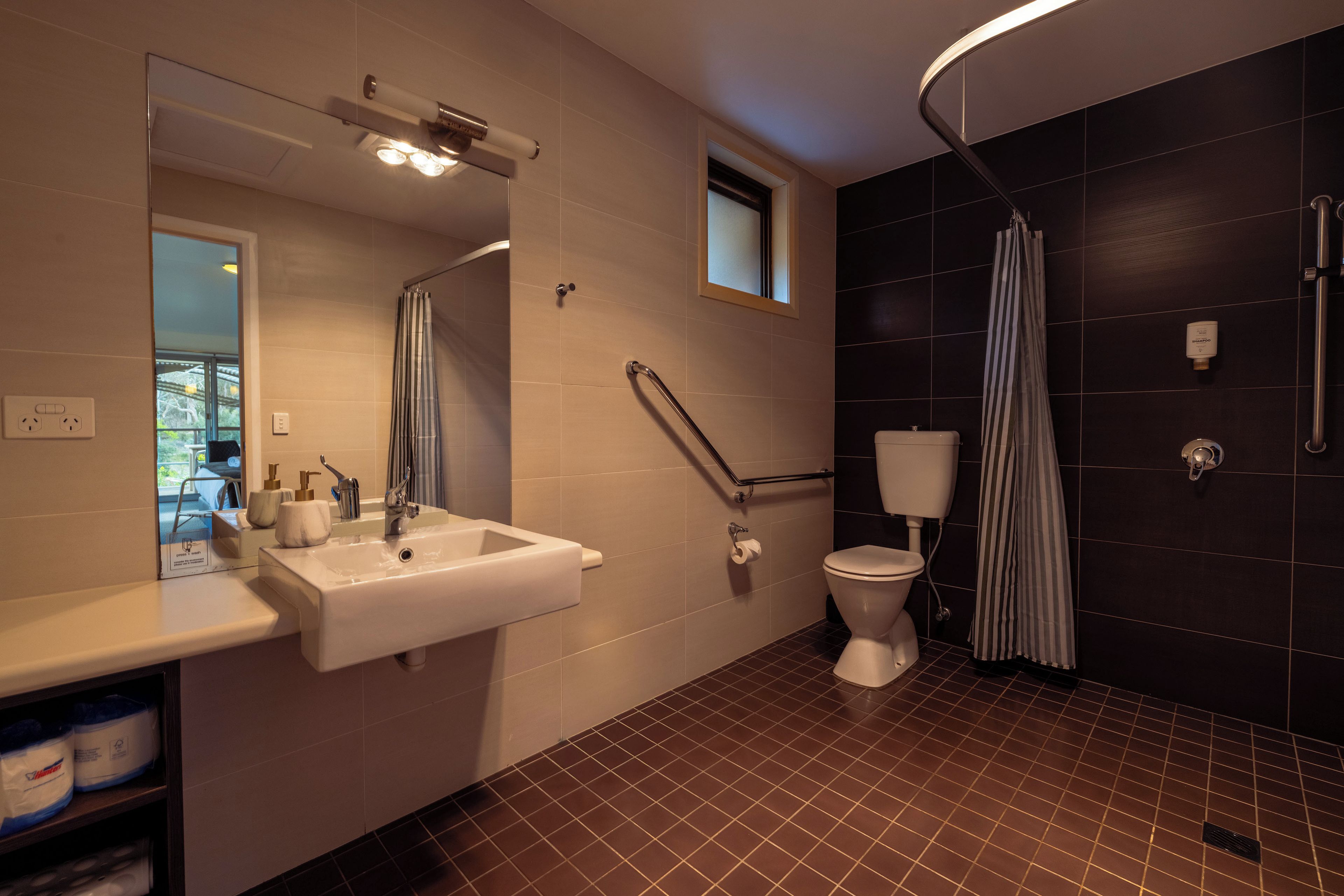 Un baño moderno con un lavamanos blanco, un espejo, un inodoro, una ducha con cortina a rayas y una ventana pequeña.