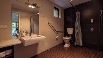 A modern bathroom with a white sink, a mirror, a toilet, a shower with a striped curtain, and a small window.