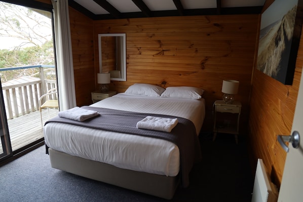 Un dormitorio con paneles de madera, una cama, dos mesitas de noche y un balcón.