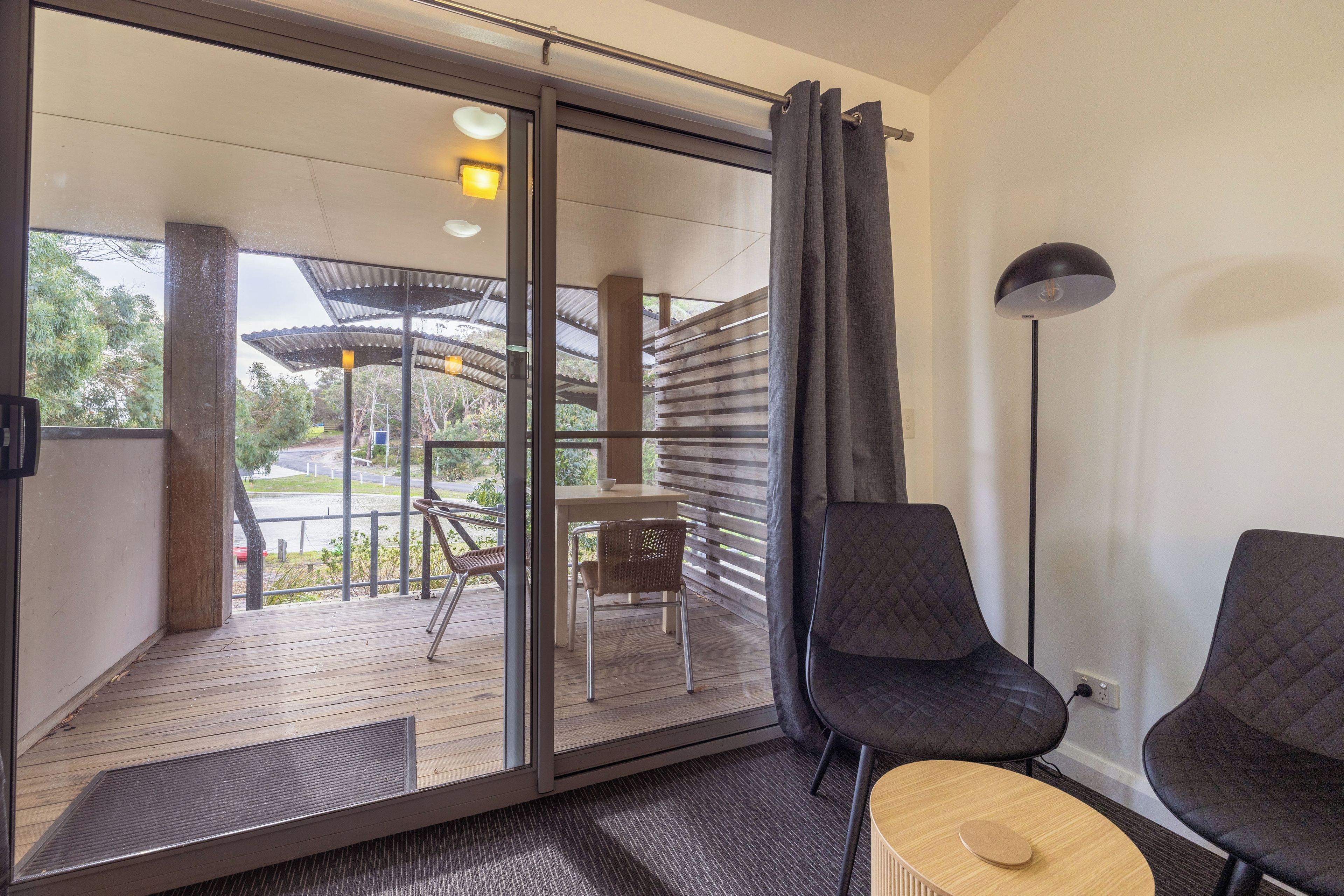 A modern room with a sliding glass door leading to an outdoor area with a wooden deck and chairs.