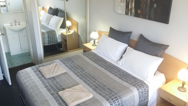 Une chambre d’hôtel bien rangée, avec un grand lit, des tables de chevet, un miroir et une salle de bain visible à travers une porte ouverte.