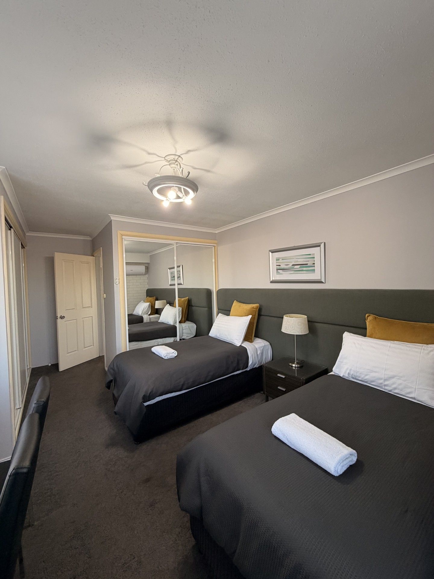 Ein Hotelzimmer mit zwei Betten, einem Deckenventilator, einer Tür und einem gerahmten Bild an der Wand.