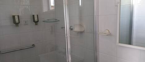 Ducha con mampara de vidrio, repisa de vidrio y barandilla.