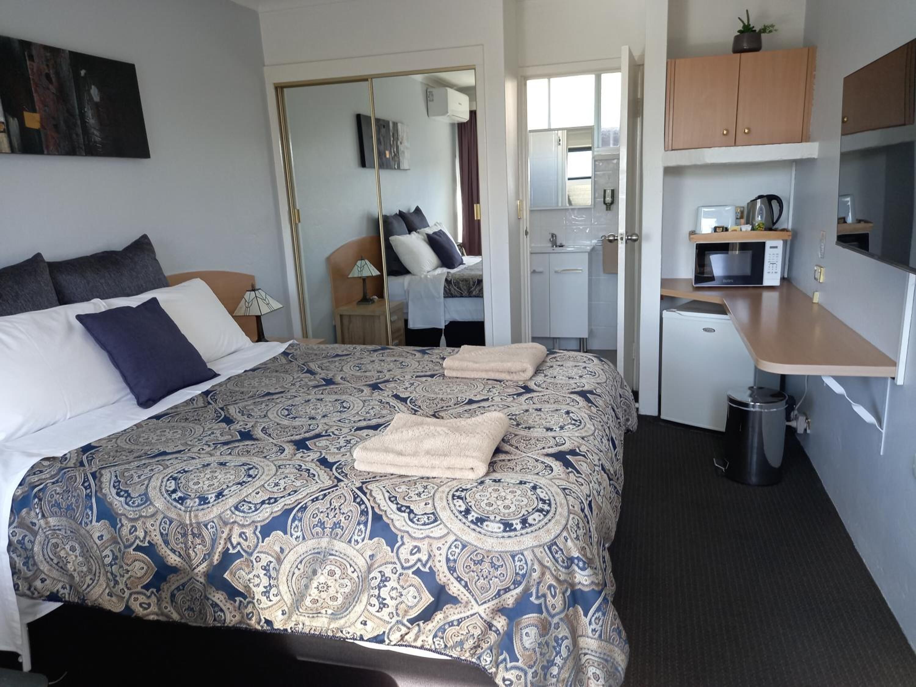 Una habitación de hotel con una cama grande, un escritorio, un microondas y una pequeña kitchenette.