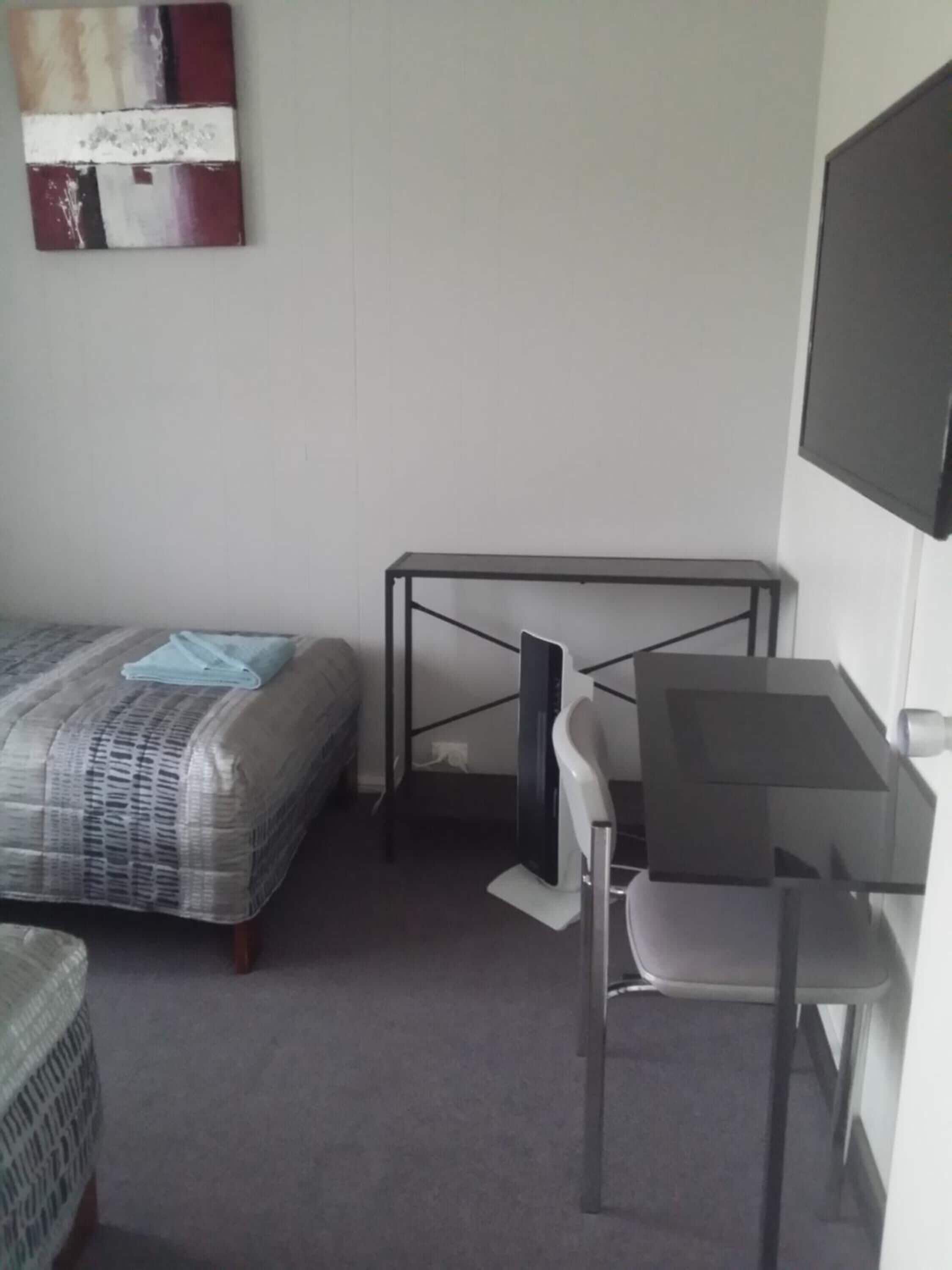 Una stanza piccola e arredata in modo essenziale, con un letto, una scrivania e una sedia.