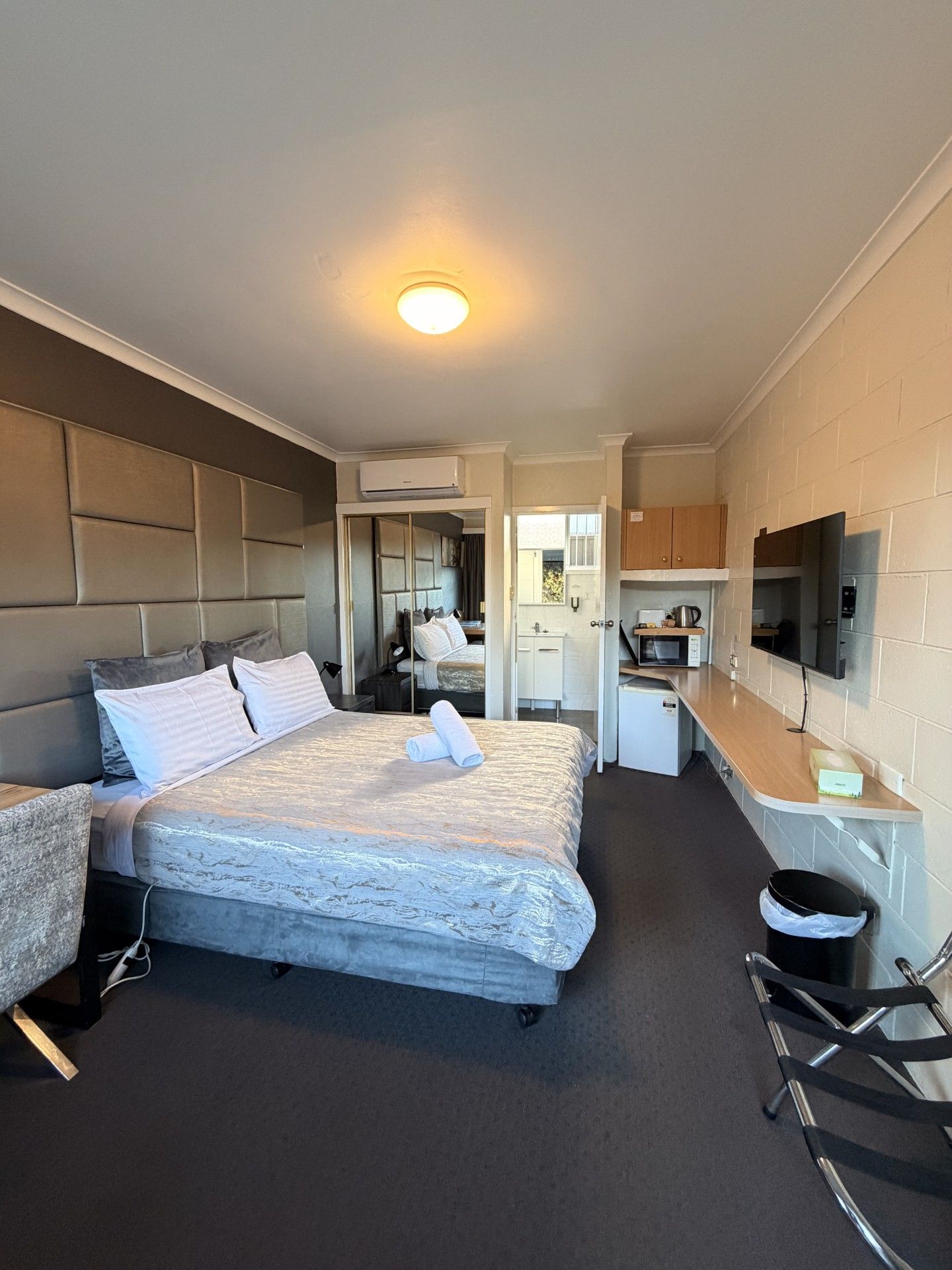 A hotel room with a bed, a desk, a kitchenette, and a television.