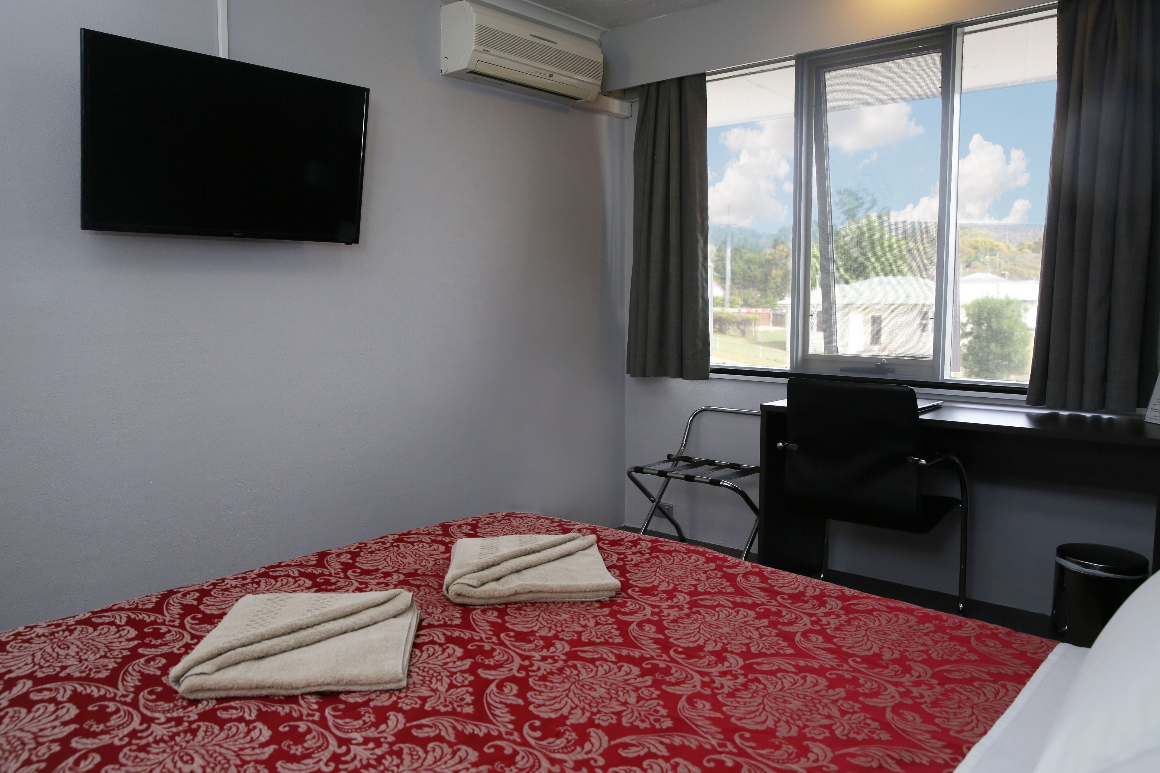 Une chambre d’hôtel équipée d’un lit, d’un bureau, d’une chaise, d’une télévision et d’une fenêtre donnant sur un paysage agréable.
