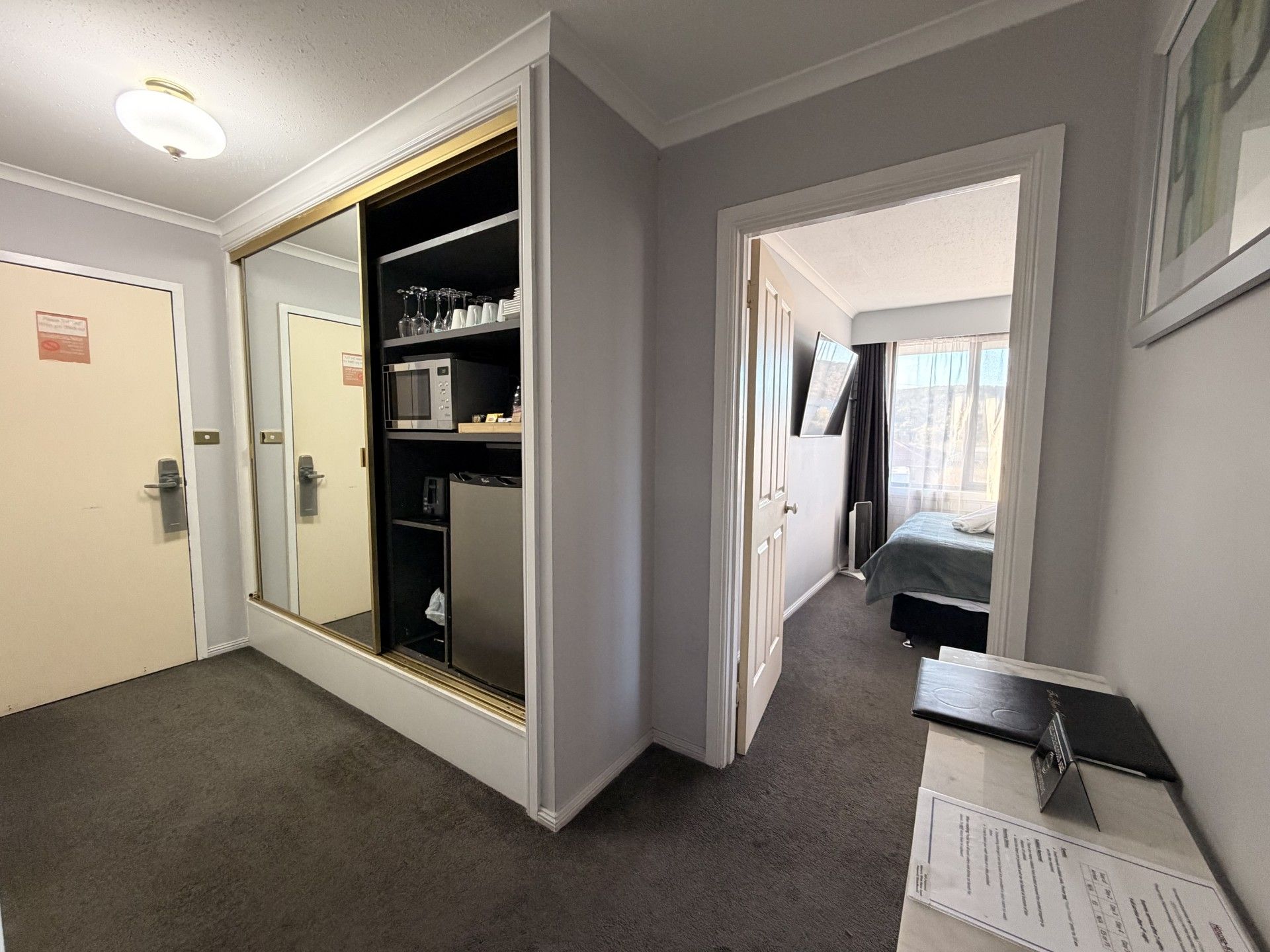 Habitación de hotel con vestidor, cama, escritorio con una laptop y vista al exterior.