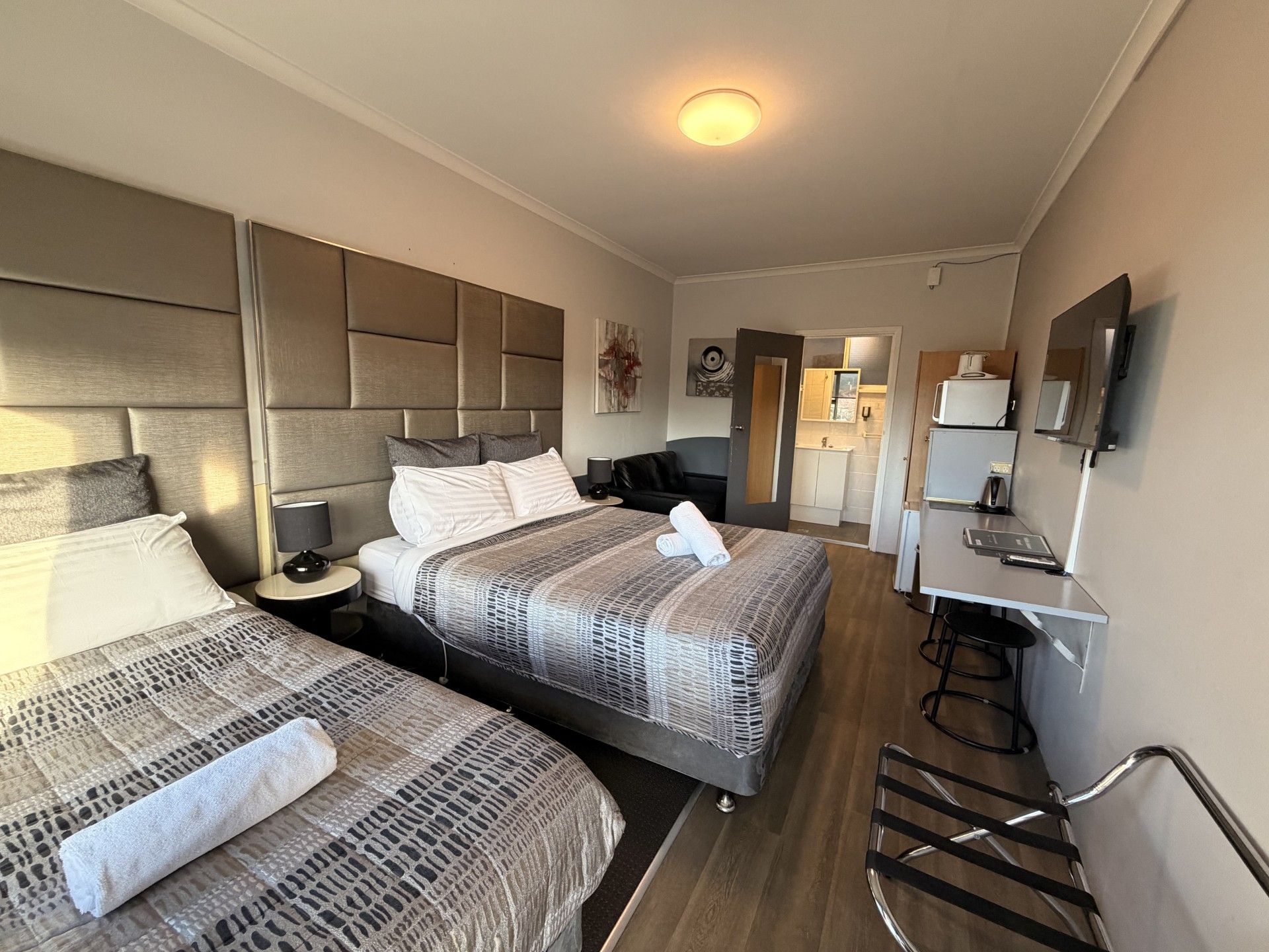 A hotel room with two beds, a desk, a chair, a TV, and a kitchenette.