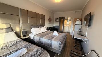A hotel room with two beds, a desk, a chair, a TV, and a kitchenette.