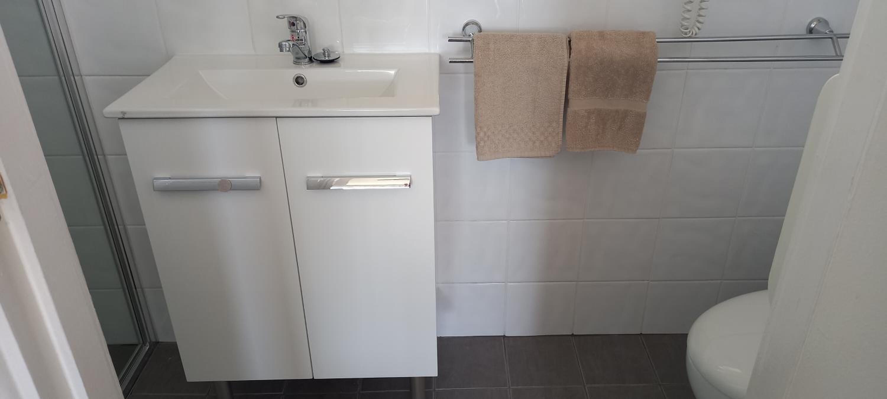 Une salle de bain avec un lavabo blanc, deux porte-serviettes et des toilettes.