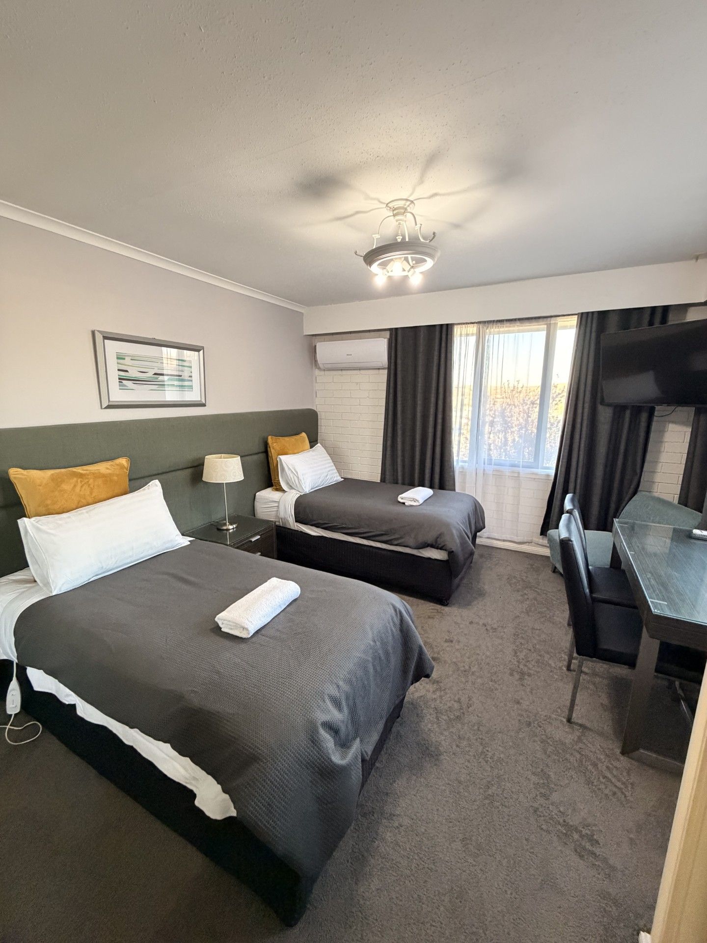 A hotel room with two beds, a desk, a television, and a window with curtains.