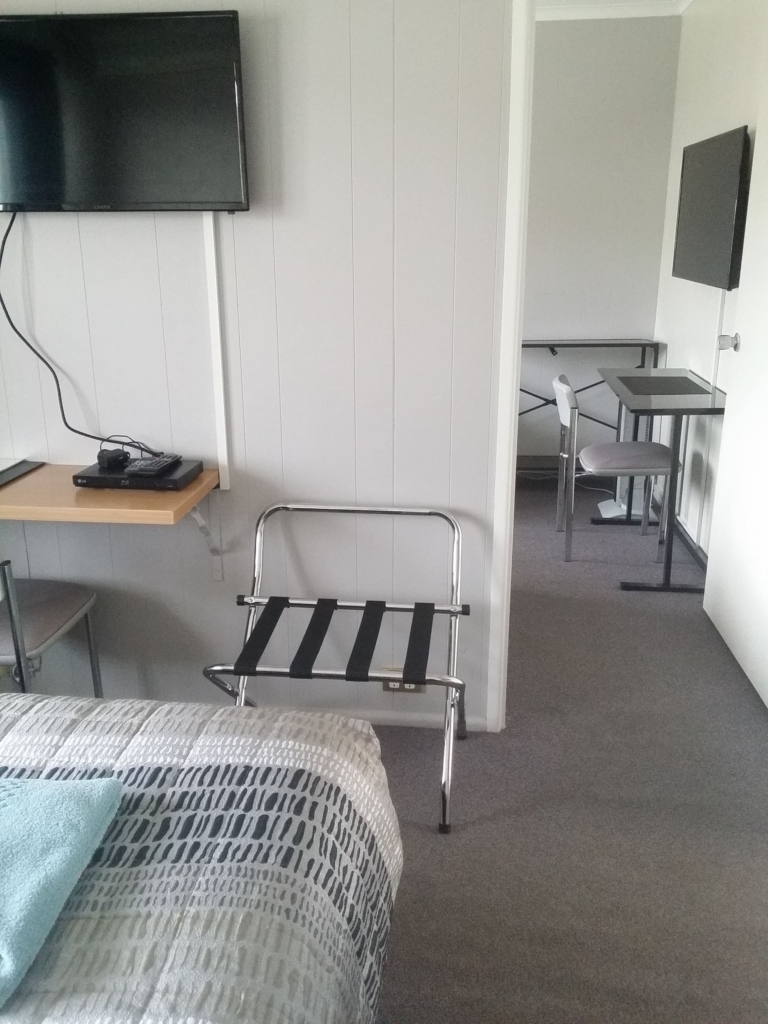Een hotelkamer met een bed, een bureau met een computer, een aan de muur bevestigde televisie en een stoel.