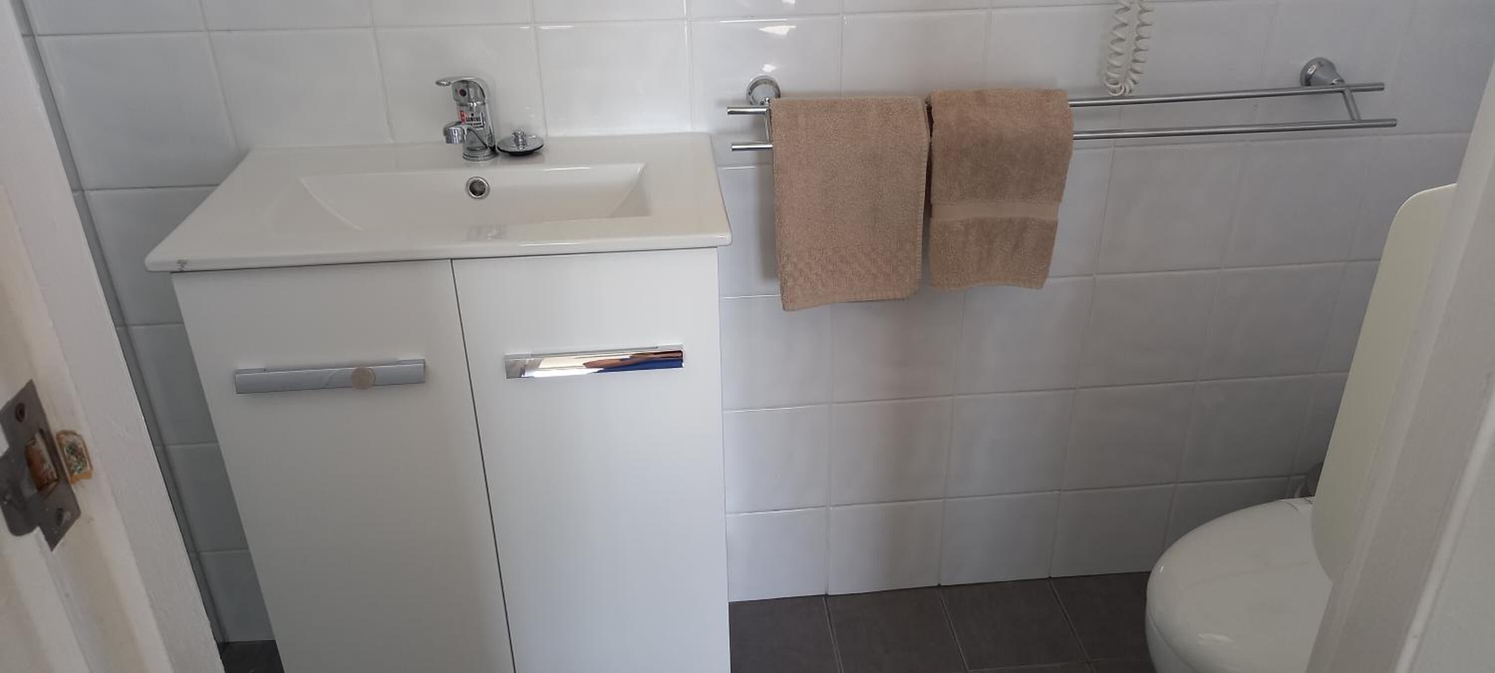 Un baño con lavamanos blanco, un espejo y un perchero con dos toallas.