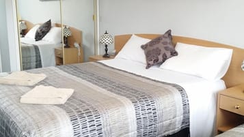 A hotel room with a large bed, a smaller bed, a wardrobe, a bedside table with a lamp, and a painting on the wall.