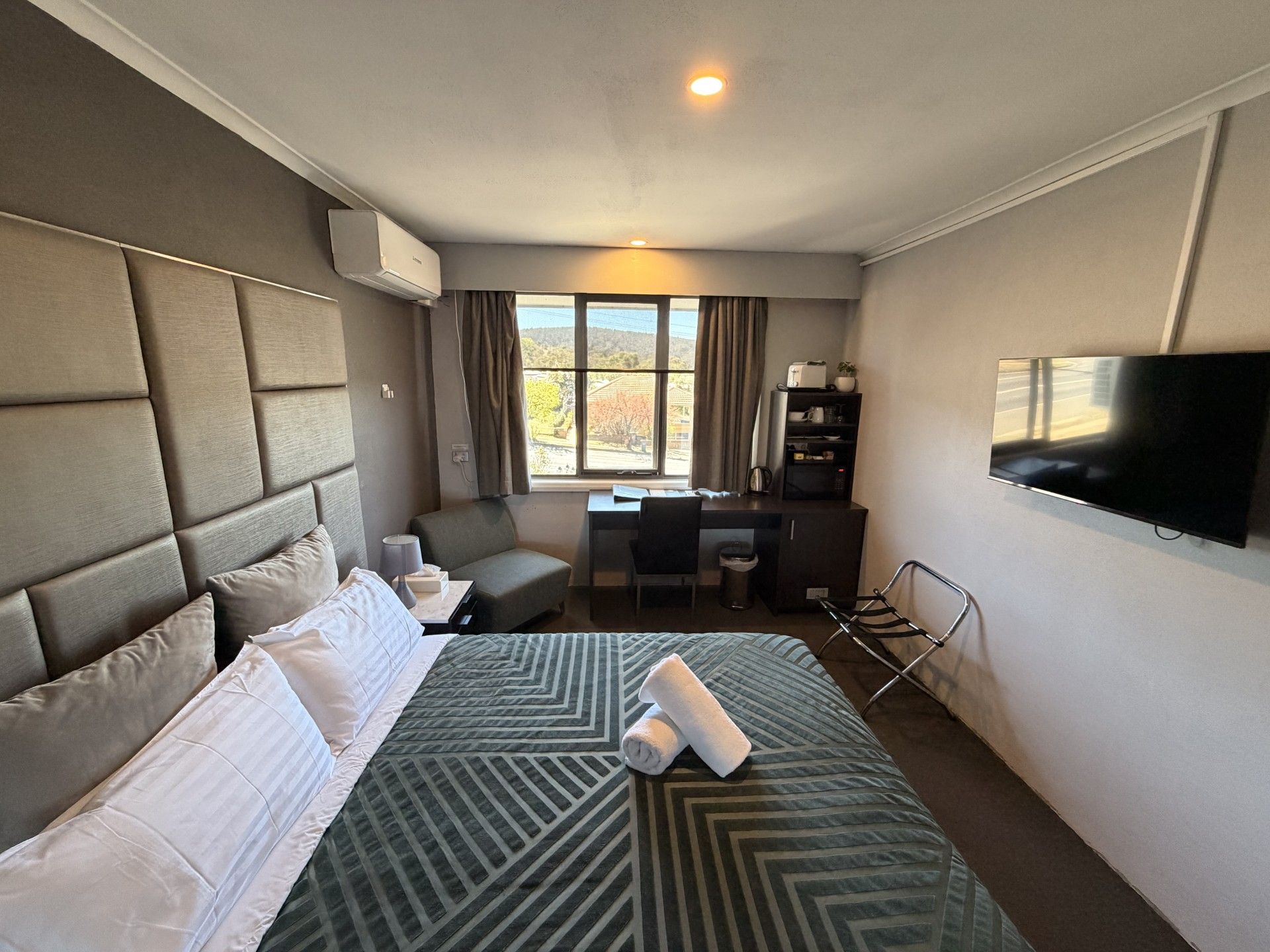 Een hotelkamer met een groot bed, een bureau, een stoel, een televisie en een raam met gordijnen.