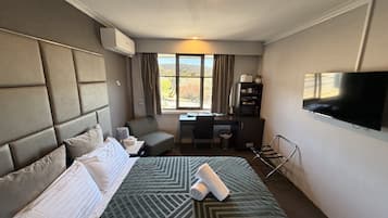 Een hotelkamer met een groot bed, een bureau, een stoel, een televisie en een raam met gordijnen.