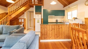 Amplia sala de estar con escalera de madera, cocina con armarios verdes y un rincón de estar acogedor.