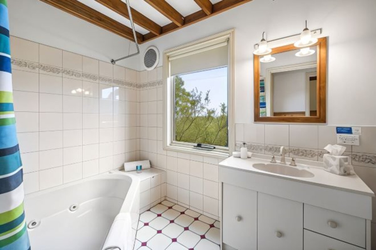 A bathroom with a bathtub, a window with a view, a vanity with a mirror, and a shower curtain.
