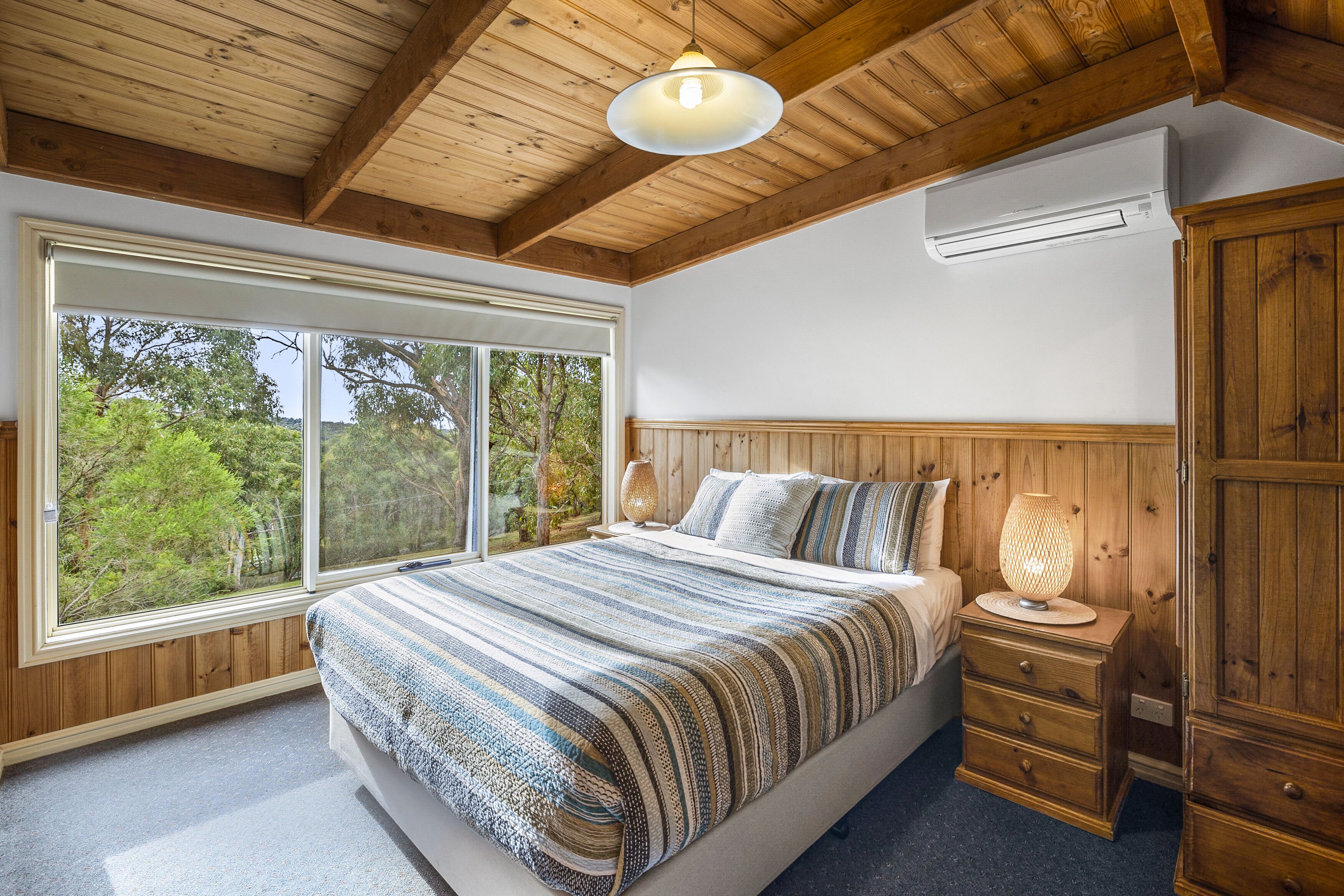 Un dormitorio con un ventanal grande, techo de madera y una cama con manta a rayas.