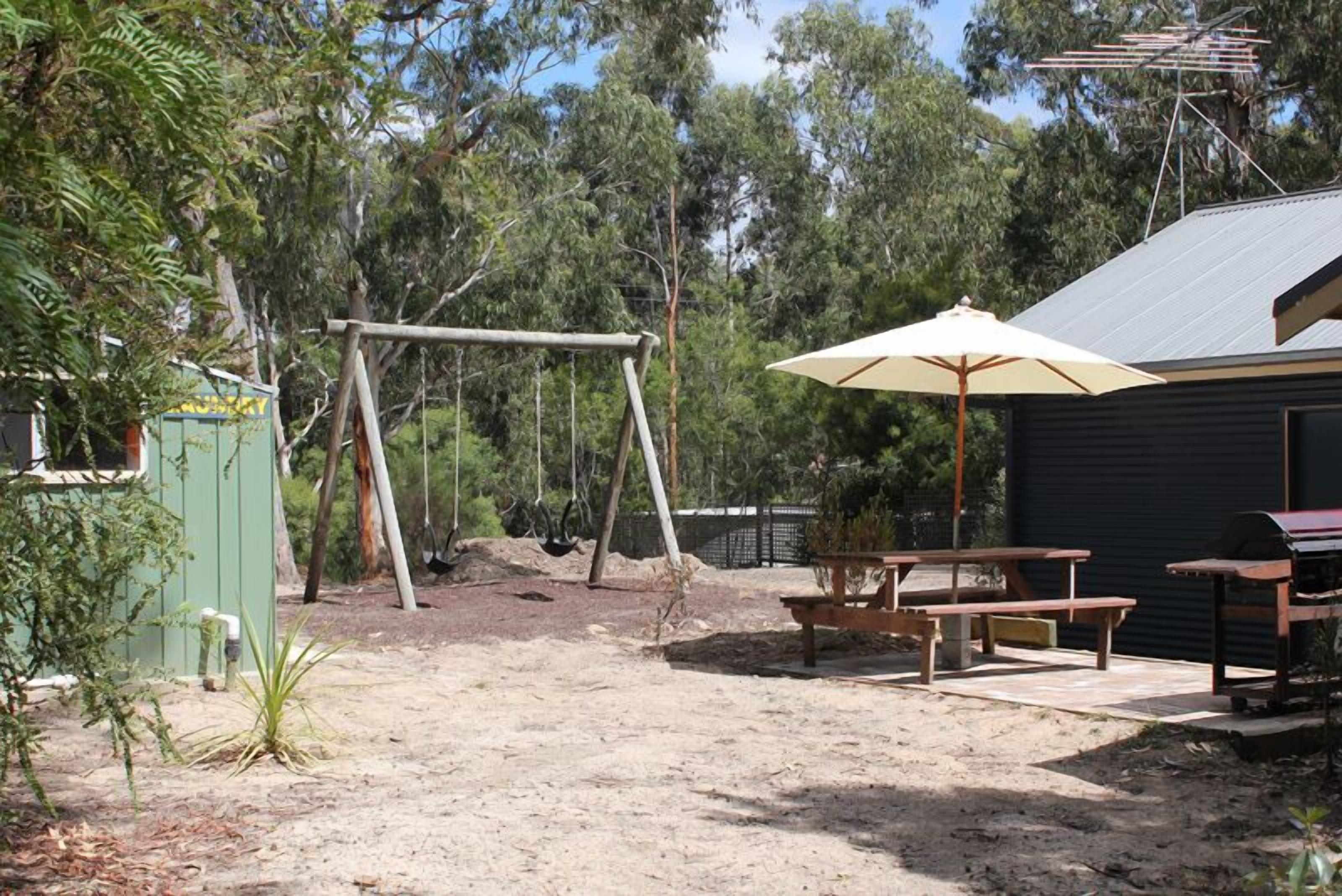 Un patio trasero con un columpio, una mesa de picnic y una sombrilla.
