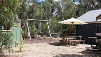 Un patio trasero con un columpio, una mesa de picnic y una sombrilla.