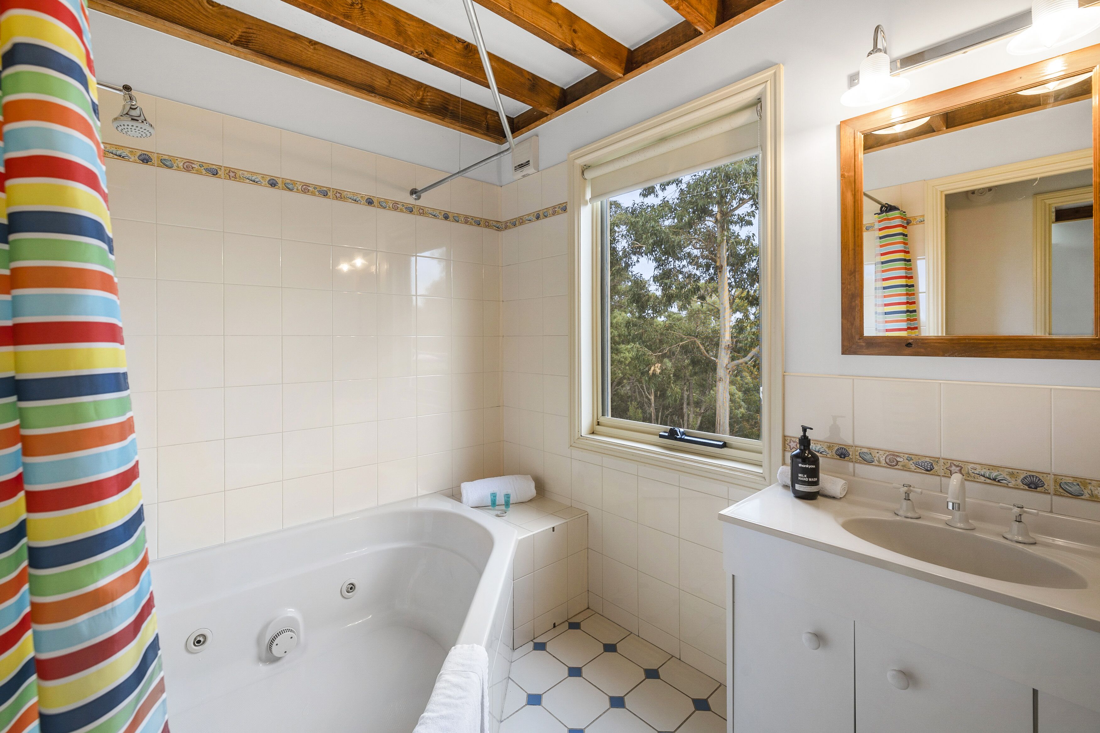 A bathroom with a bathtub, a window, a sink, and a mirror.