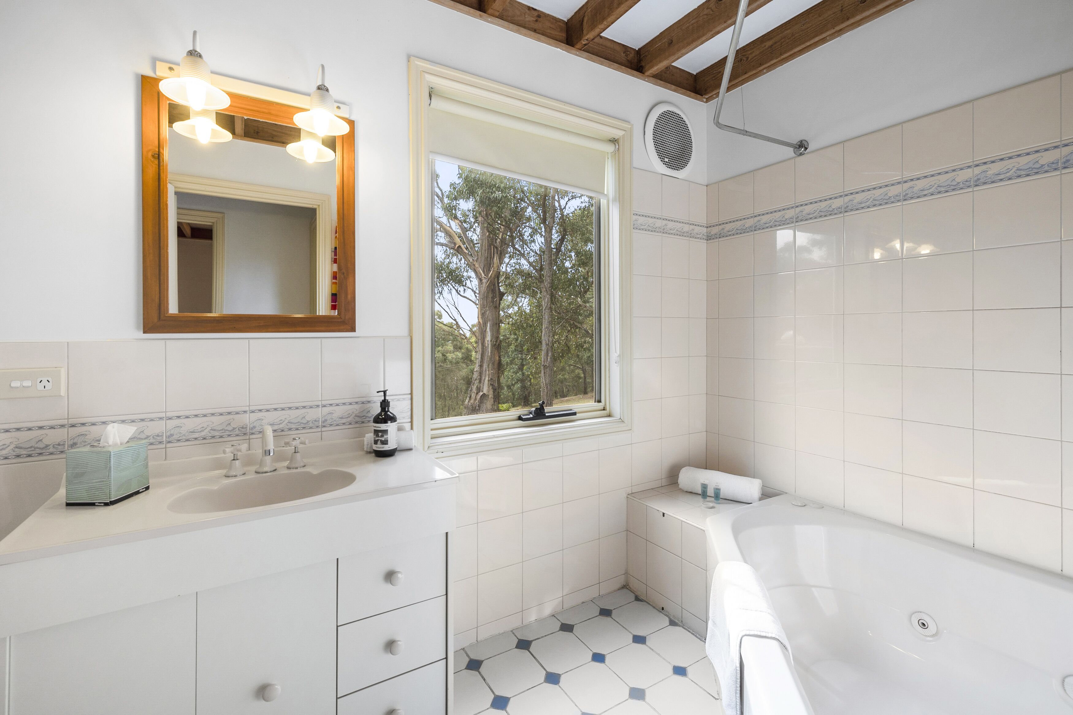 A modern bathroom with a large mirror, a sink, a bathtub, and a window with a view of trees.