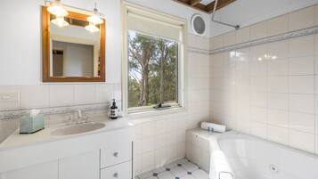 A modern bathroom with a large mirror, a sink, a bathtub, and a window with a view of trees.