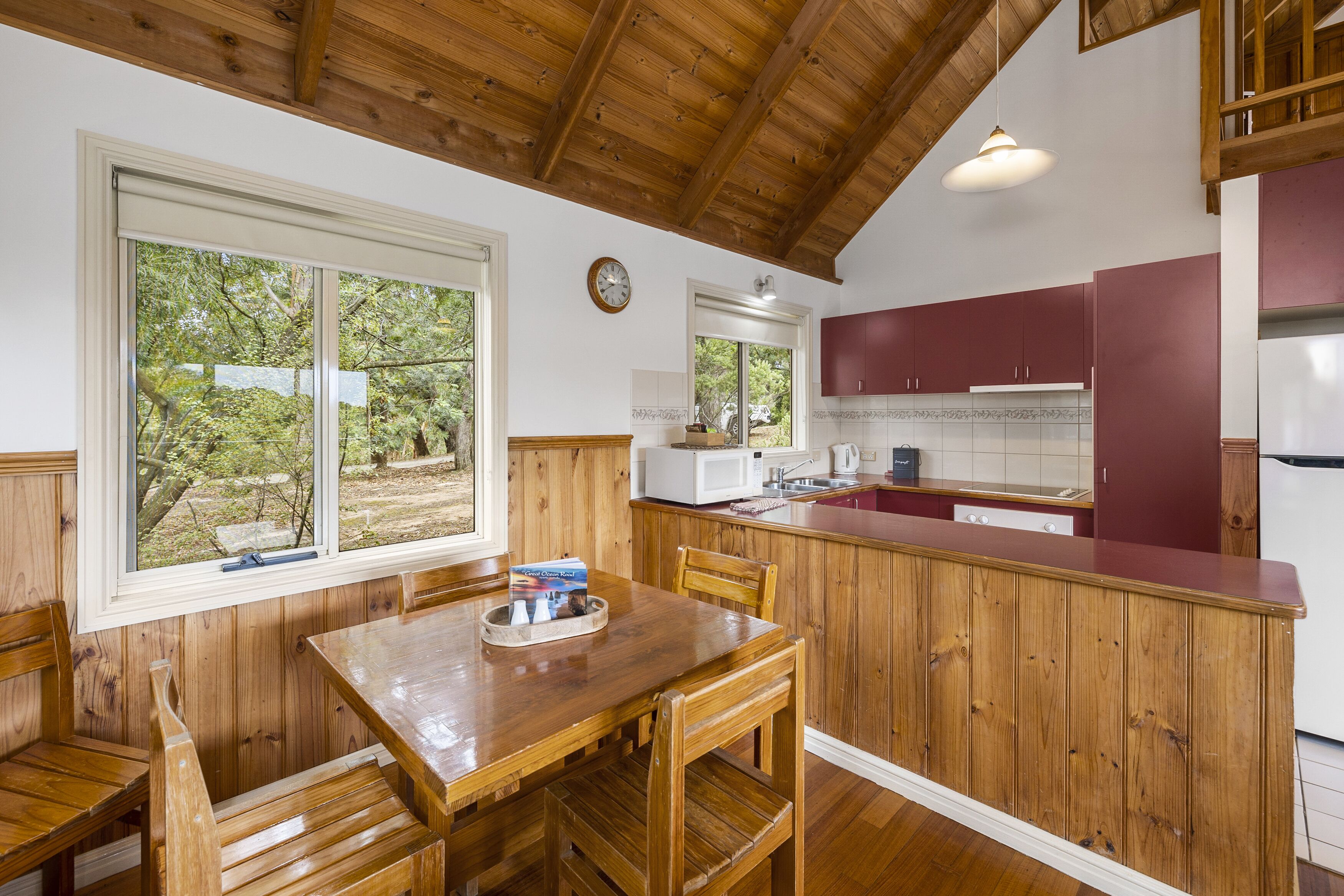 A wooden kitchen with a dining area, featuring a large window, wooden cabinets, and a white refrigerator.