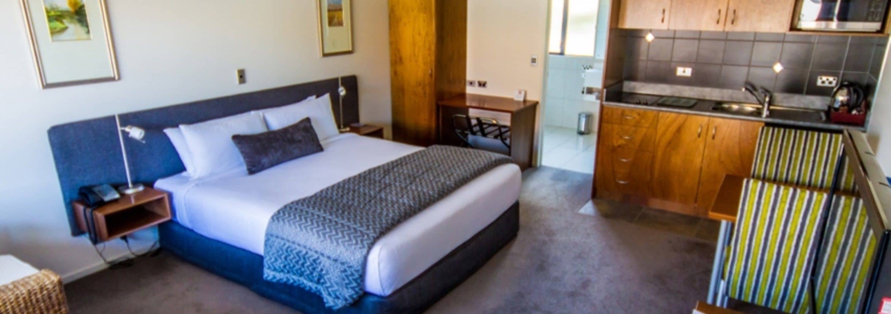Una habitación de hotel con cama, mesita de noche y zona de kitchenette.