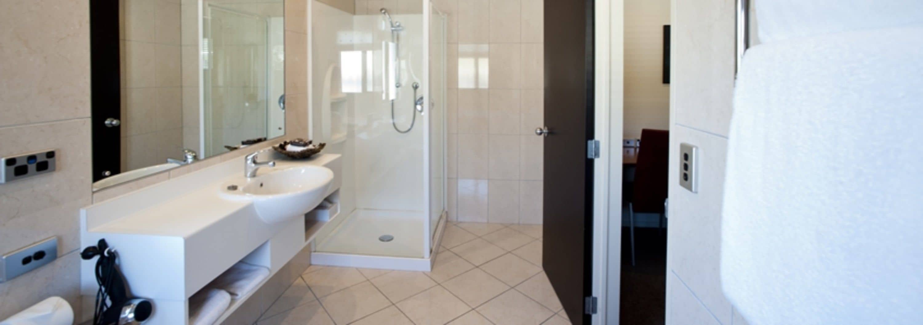 Un baño moderno con un espejo grande, un lavamanos y una zona de ducha.