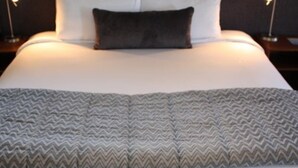 A neatly made bed with a patterned blanket, two bedside tables with lamps, and a dark-colored pillow. - Harvest Lodge (Havelock North)