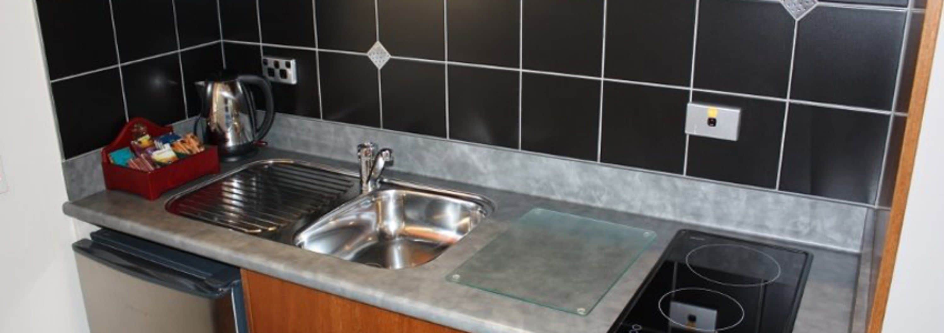 Una cocina con un lavamanos de acero inoxidable, una tetera y un tostador.