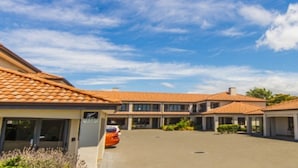 A hotel with a spacious courtyard, multiple buildings with tiled roofs, and a clear blue sky. - Harvest Lodge (Havelock North)