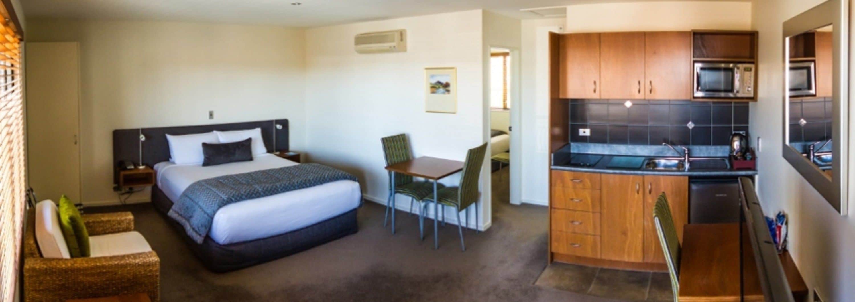 Een hotelkamer met een bed, een bureau, een stoel en een kitchenette met een magnetron en een wasbak.