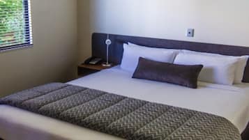 Una cama bien tendida con una colcha estampada, una lámpara de noche y una mesita de noche con un teléfono.