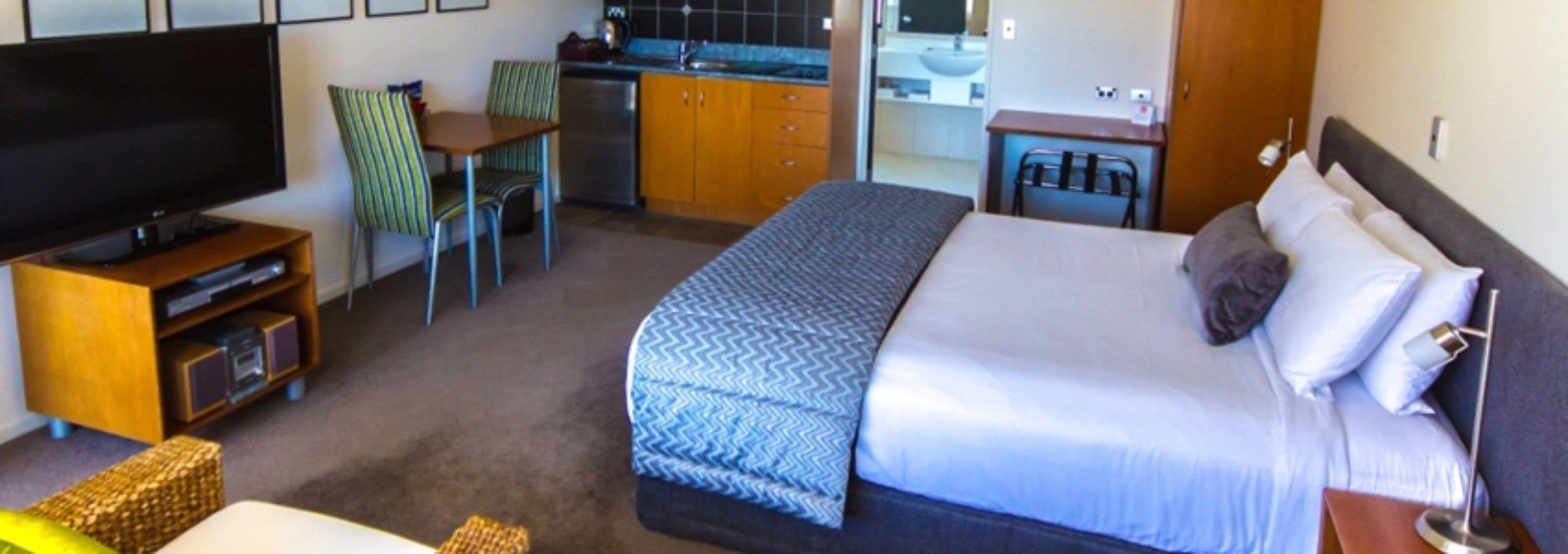 A hotel room with a bed, a TV, a kitchenette, and a seating area.