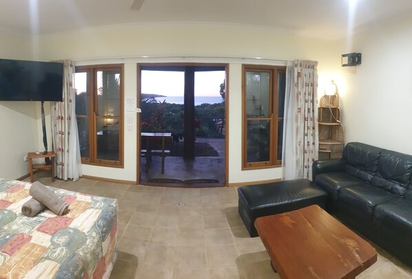 Una sala de estar con un sofá, una mesa de centro de madera, una cama con colcha y un televisor en la pared.