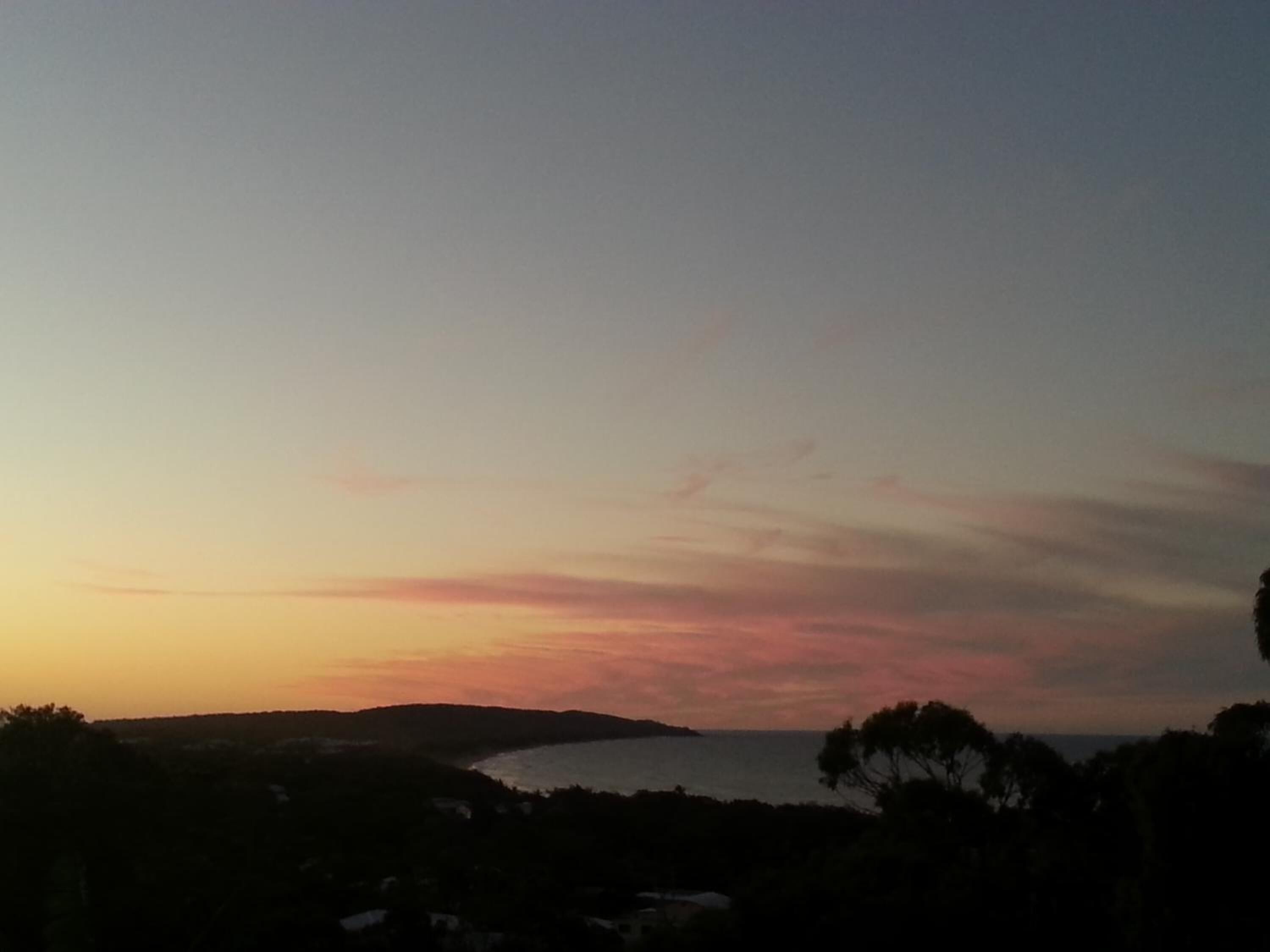A coastal landscape during sunset with a view of the sea and distant hills.