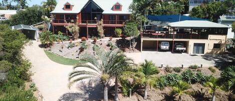 A two-story building with a red facade, a covered parking area, and a landscaped garden with palm trees.