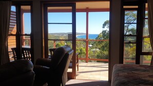 A room with a bed, a chair, and a view of the sea through large windows.