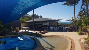 A pool area with a covered patio, outdoor seating, and a view of the ocean.