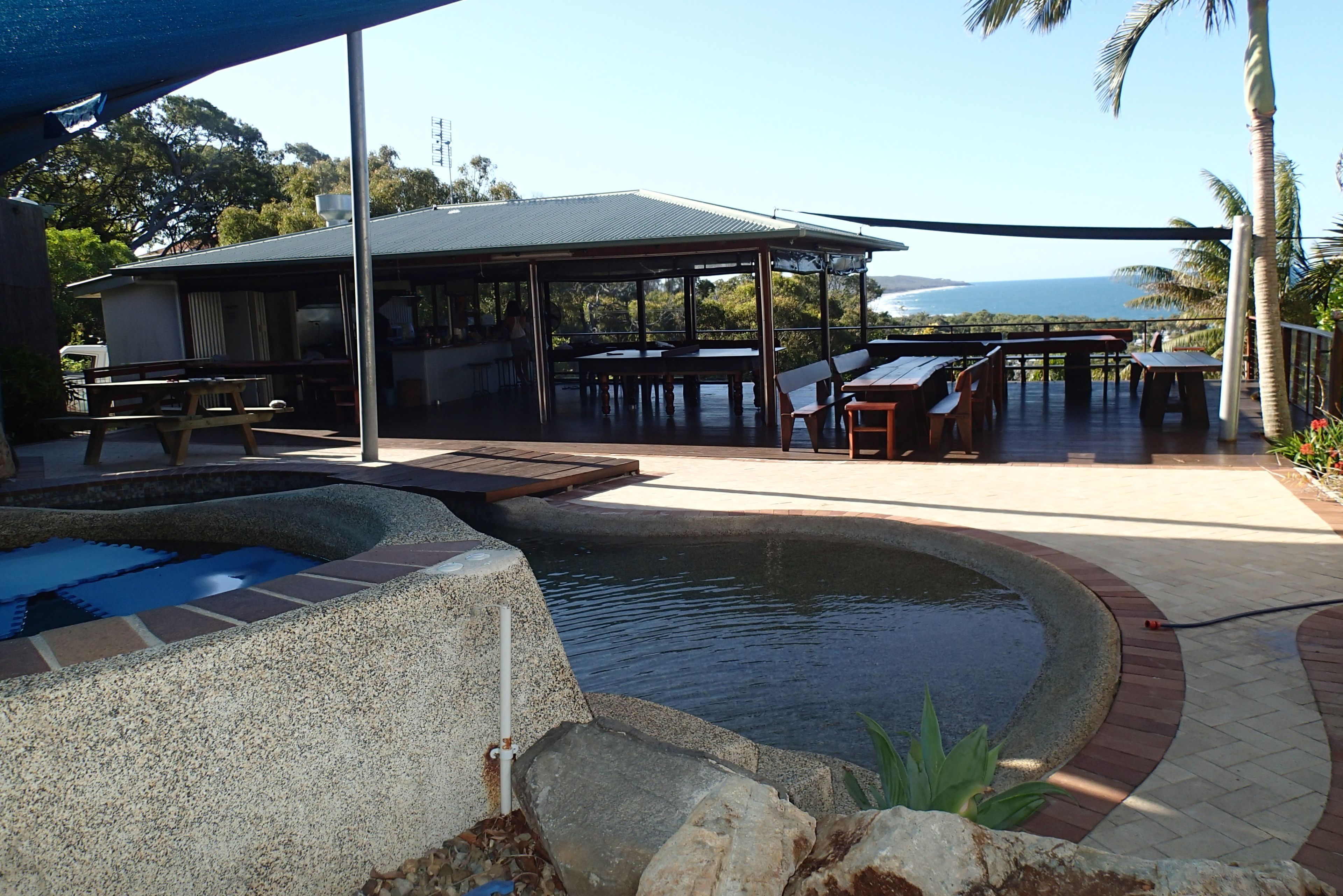 An outdoor pool area with a covered seating area and a view of the ocean.